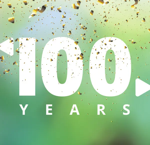 En grön bakgrund med guldfärgat konfetti som singlar ner ovanifrån över en vit 100års logotyp.