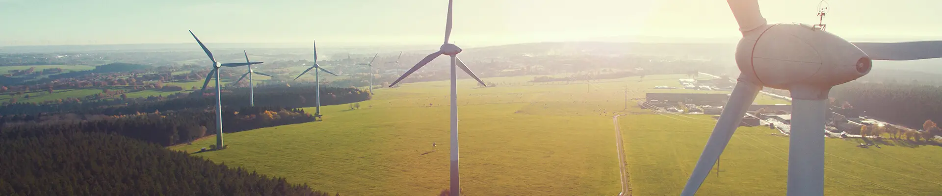 En vindkraftsturbin med flera vindkraftverk i bakgrunden med utsikt över stora fält.