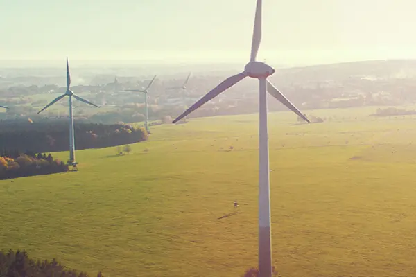 A wind turbine with several wind turbines in the background overlooking large fields.