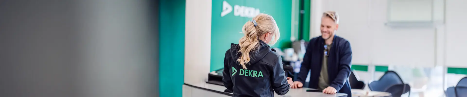 En kvinna och en man står och pratar över en kassadisk med en grön vägg i bakgrunden.