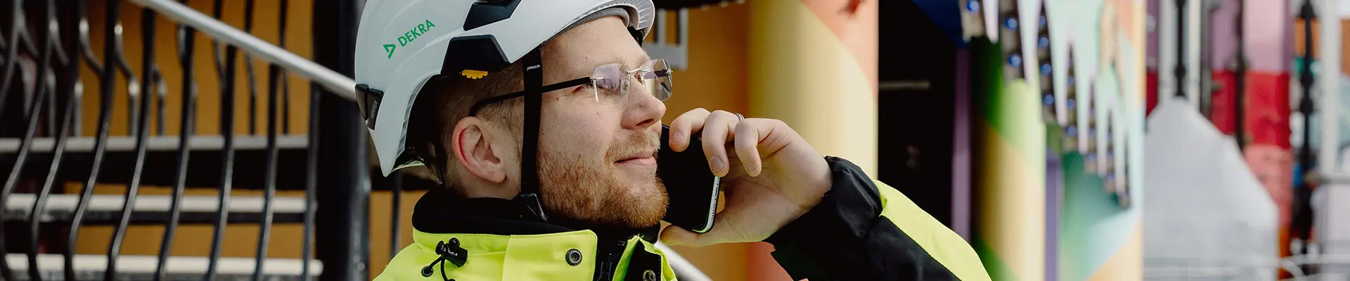 En man i reflexkläder och vit hjälm som tittar åt höger och pratar i en mobiltelefon. En man i reflexkläder och vit hjälm som tittar åt höger och pratar i en mobiltelefon.