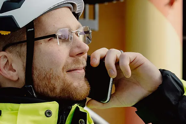 A man in reflective clothing and a white helmet looking to the right and talking on a mobile phone.