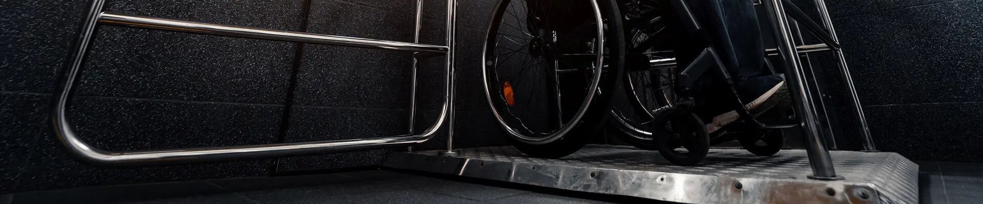  En man sitter i rullstol ovanpå en lågfartshiss och ska stänga grinden till hissen. 