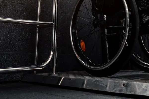 A man sits in a wheelchair on top of a low-speed elevator and is about to close the gate to the elevator.