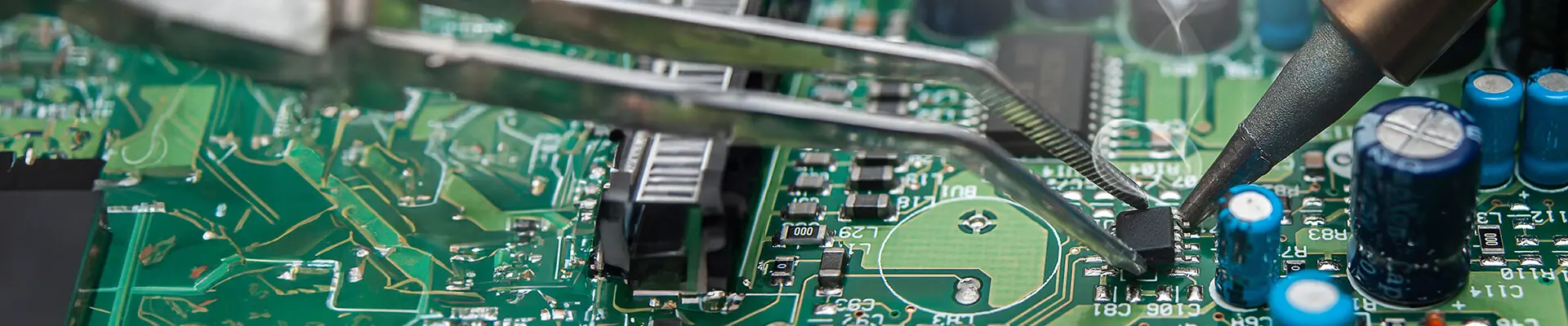 Close-up of a solderer soldering to a green circuit board.