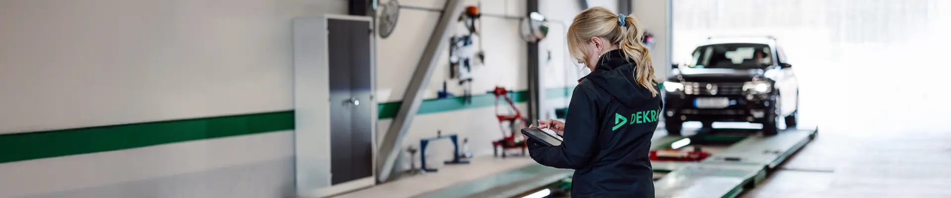 A woman holding a tablet with a black car in the background. A woman holding a tablet with a black car in the background.