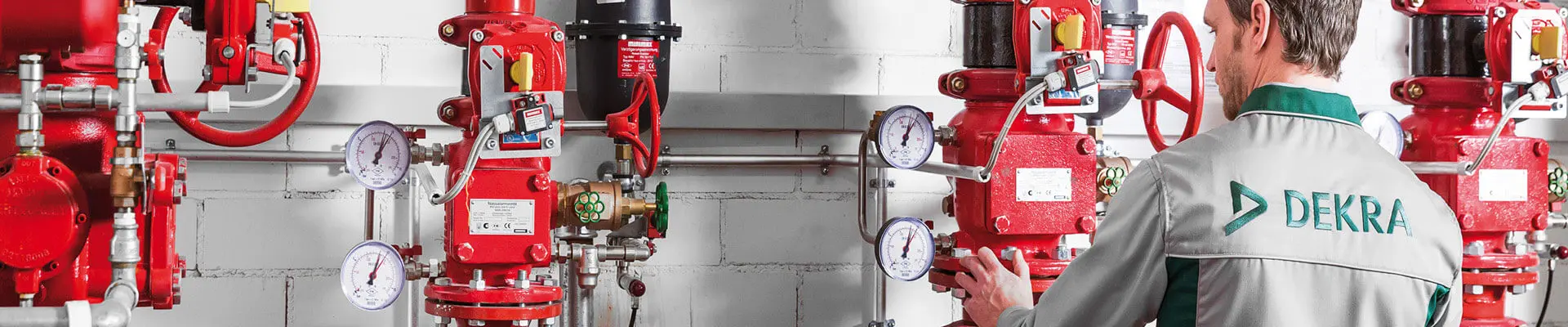 En man i arbetskläder står och inspekterar flera röda rör med tryckluft och tryckmätare på.
