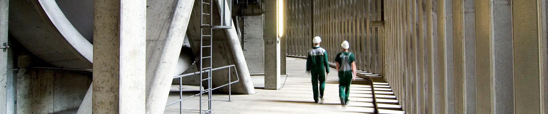  Ett par går sida vid sida i en korridor med högt tak byggt helt i betong.