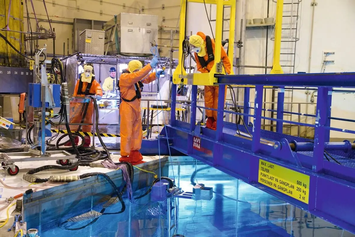 Inspectors dressed in orange overalls performing testing at a reactor pool. Inspectors dressed in orange overalls performing testing at a reactor pool.
