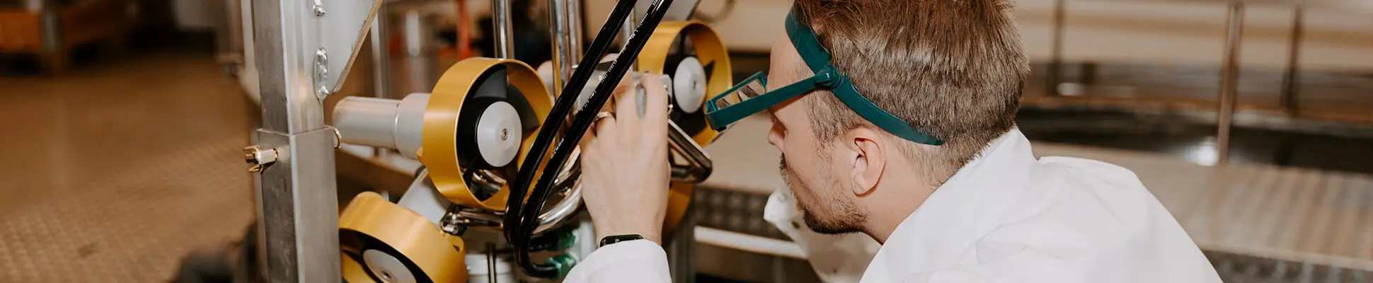  En man i skyddsglasögon observerar en komplex maskin som visar upp nyfikenhet och engagemang i teknik.