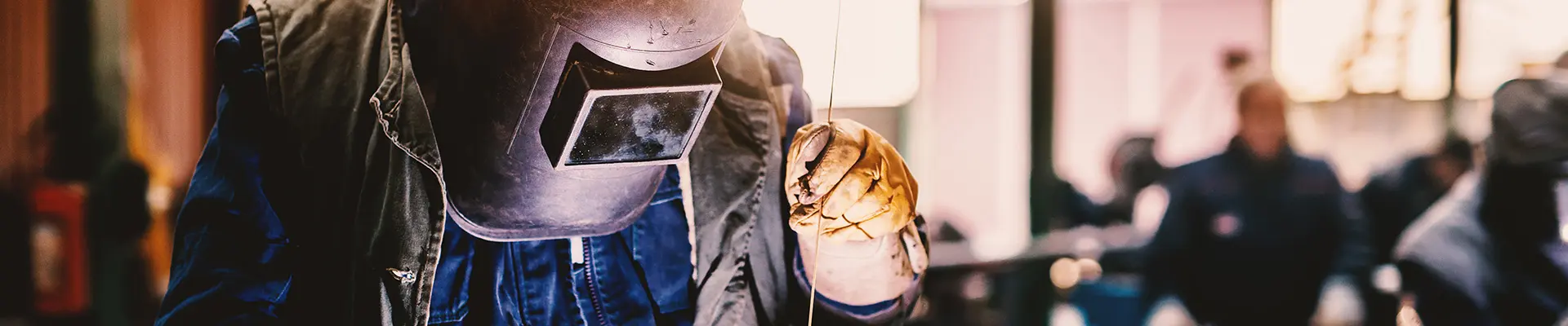  En man i skyddsutrustning som hjälm och jacka står över ett föremål som ska svetsas i en industriell fabrik.