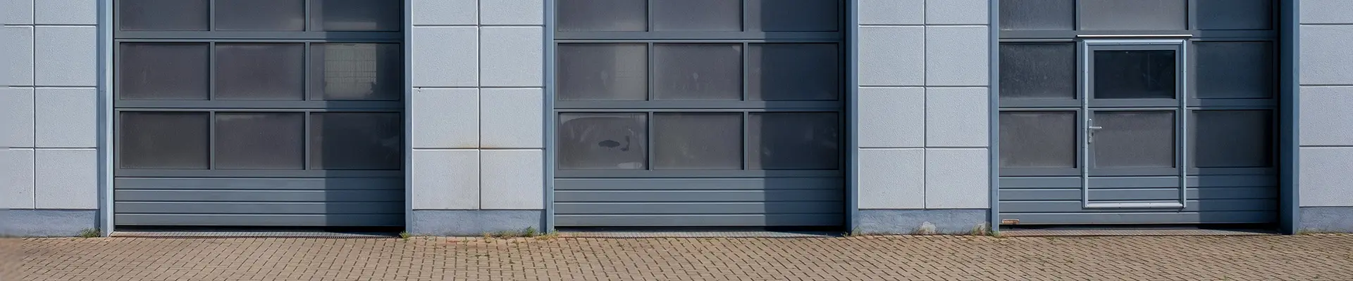  På den grå fasaden av ett hus så ser man tre grå garageportar.