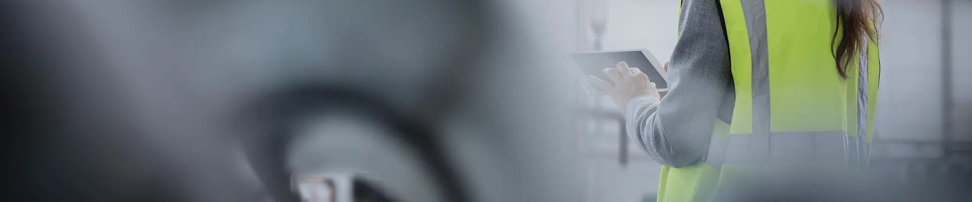 A person carrying out a risk assessment in the work environment wearing a reflective vest with an iPad in hand.