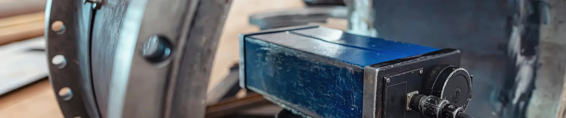  Närbild av en maskin i metall med olika mekaniska komponenter och en blå rektangulär del i fokus.