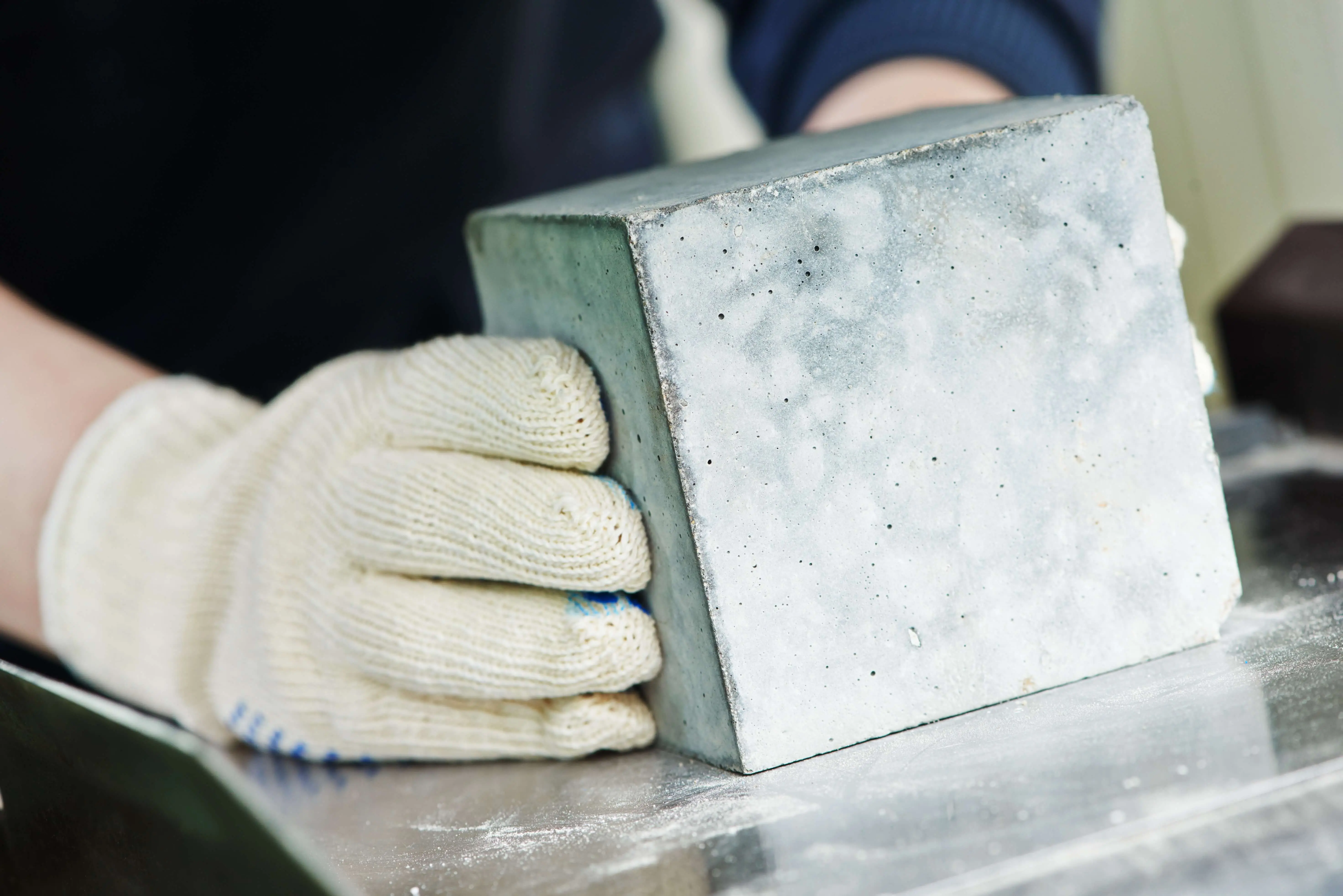 Concrete cube with a worker's hands wearing gloves.