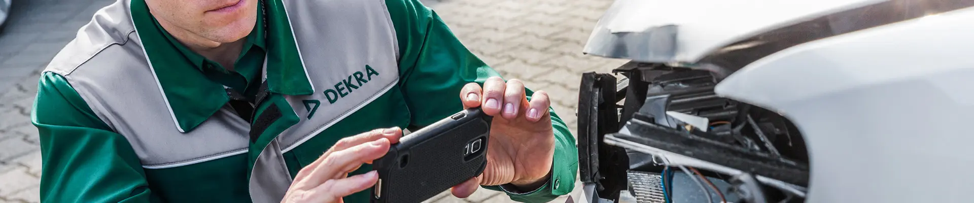  En man klädd i en grön skjorta observerar en bil med en skada på, han fotograferar även skadan med en mobiltelefon. 