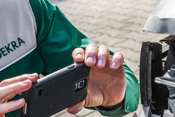  A man wearing a green shirt observes a car with damage on it, he also photographs the damage with a mobile phone.