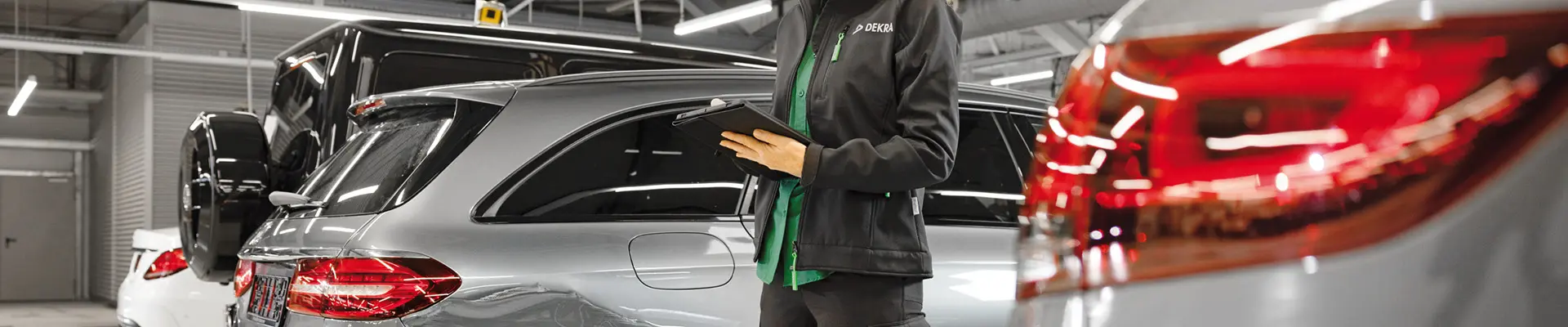 A woman in black work clothes standing among cars in a garage.