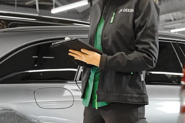 A woman in black work clothes standing among cars in a garage.