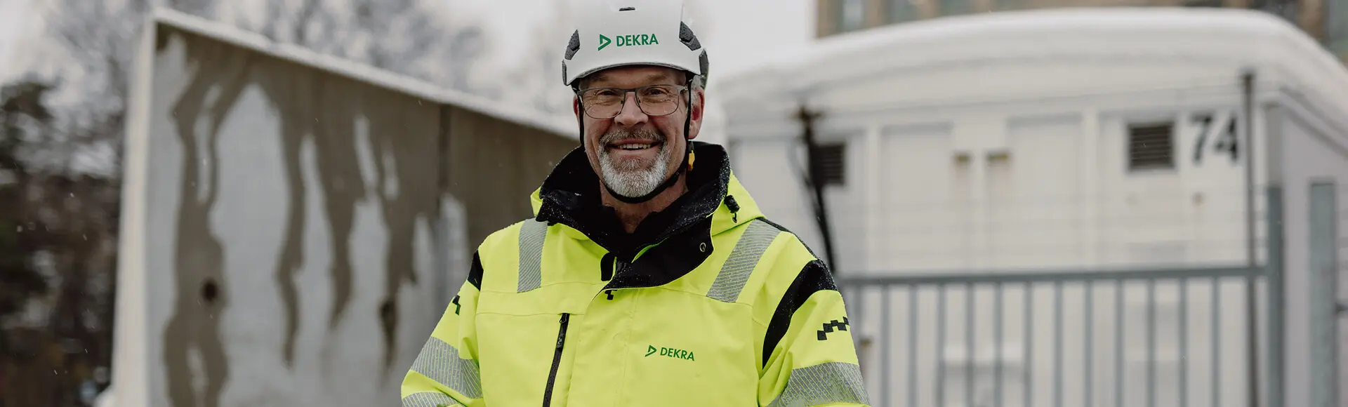 En man i reflekterande arbetskläder och vit hjälm som ler.