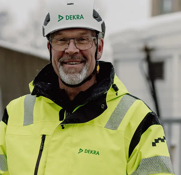En man i reflekterande arbetskläder och vit hjälm som ler.