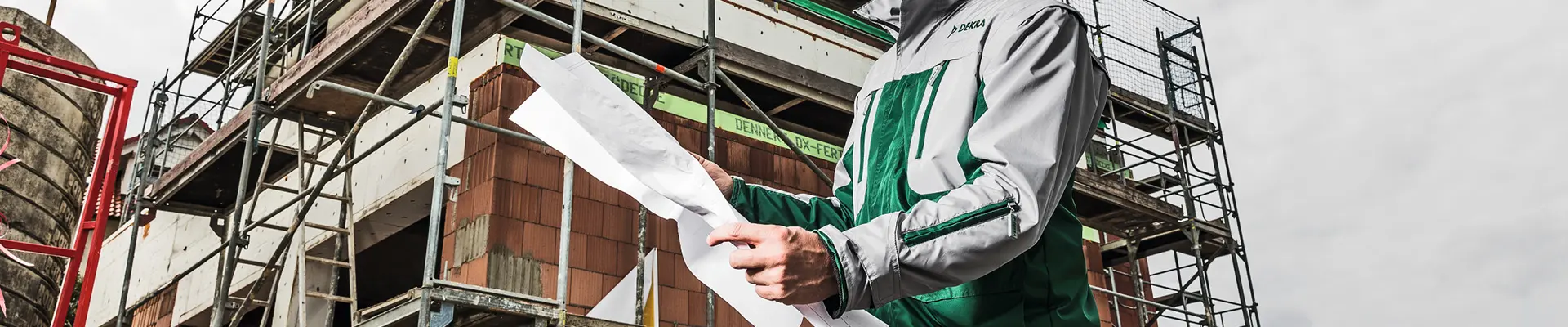  A man holding a blueprint of a steel structure is standing in front of a building that has scaffolding built around the building.