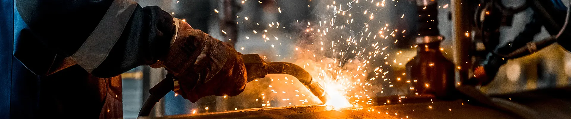 En persons hand som håller i ett svetsverktyg och svetsar så gnistor flyger. En persons hand som håller i ett svetsverktyg och svetsar så gnistor flyger.