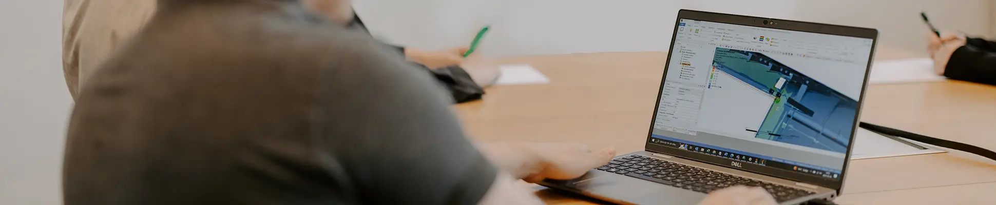 Flera personer sitter vid ett bord i ett konferensrum där en man sitter vid en laptop och visar upp digitala ritningar av tåg.