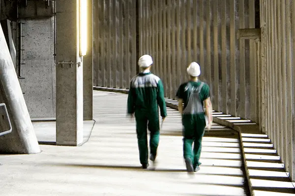 Two people walk through a corridor built entirely of concrete with a high ceiling and pillars. Two people walk through a corridor built entirely of concrete with a high ceiling and pillars.