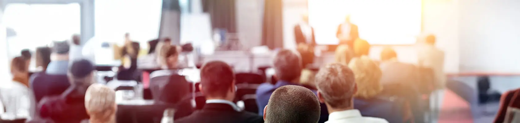 A group of people sit in a classroom and listen to the trainers giving a lecture.