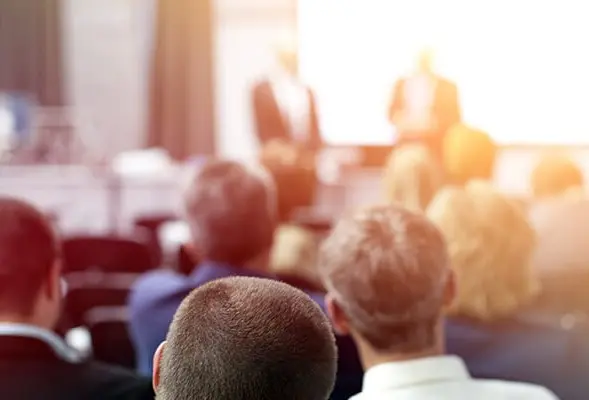 En grupp människor sitter i ett klassrum och lyssnar på utbildarna som håller i en föreläsning. En grupp människor sitter i ett klassrum och lyssnar på utbildarna som håller i en föreläsning.