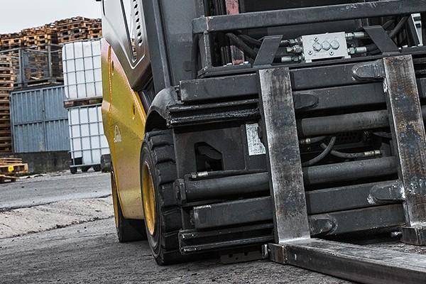 A forklift parked beside a tall stack of wooden pallets in a warehouse setting, showcasing industrial equipment and storage.