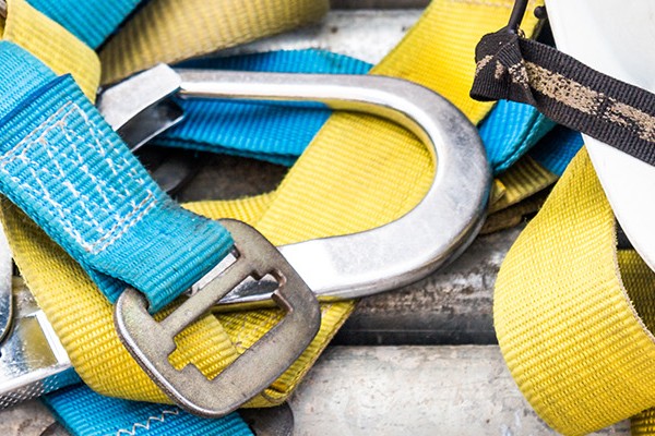 Safety equipment, including a harness and a white helmet, placed on metal pipes, highlighting the importance of protective gear when working at heights.