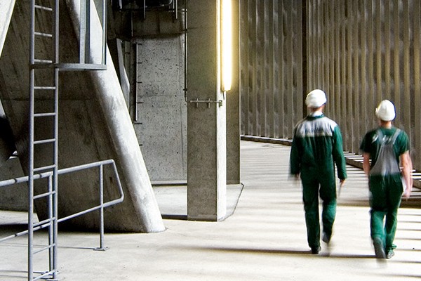  A couple walks side by side in a high-ceilinged corridor built entirely of concrete.