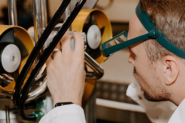 A man in goggles observes a complex machine, showcasing curiosity and engagement with technology.