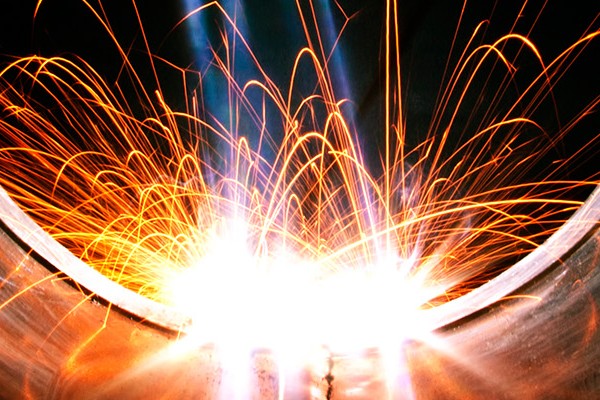 Close-up of bright sparks erupting from a metal pipe, illuminating the surrounding area with a fiery glow. 