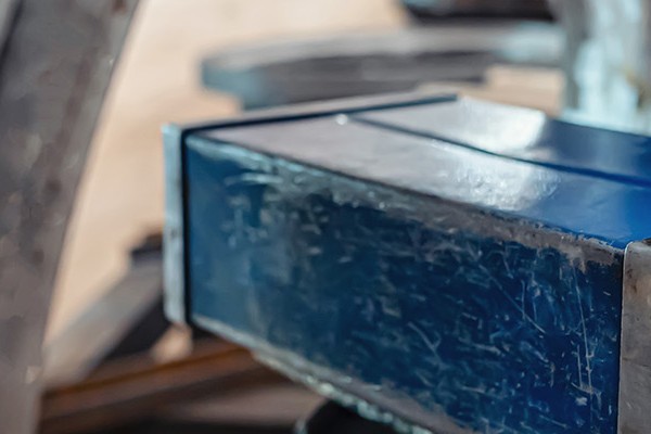 Close-up image of a metalworking machine with various mechanical components and a blue rectangular part in focus.