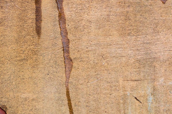 Close-up of a weathered, rusted metal surface. The image shows a mix of rust spots and peeling paint, revealing various textured layers and shades of brown, orange, and blue.