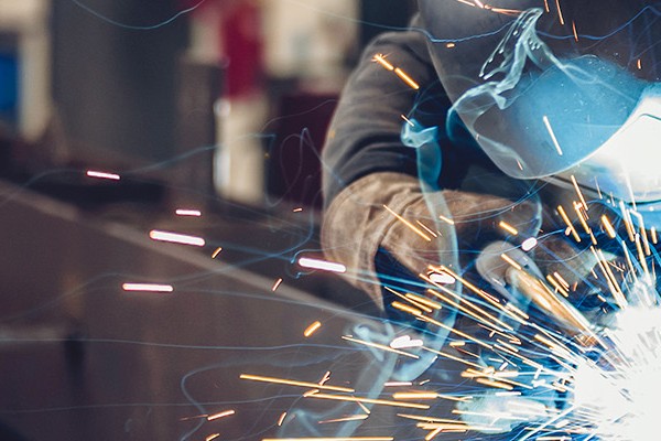 An industrial setting showcasing a welder, with bright sparks and smoke rising as metal is fused together in the factory.