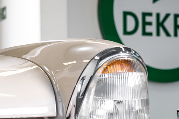 A woman sits in front of a car, with a sign that reads "DEKRA," showcasing her engagement with automotive services.