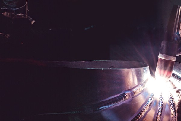 Close-up of a welder in a mask welding different parts of a thick titanium tube together.