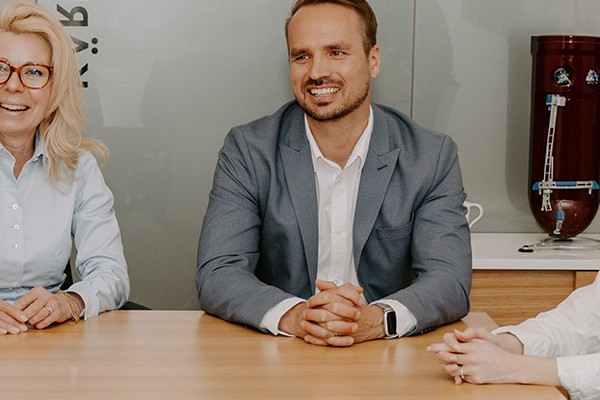 Several employees sitting at a table in a conference room, smiling and looking at each other.