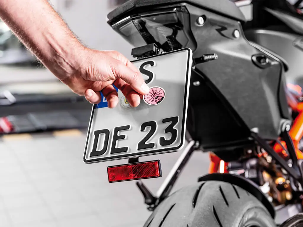 Une main appose une plaque de contrôle sur une plaque d'immatriculation de moto