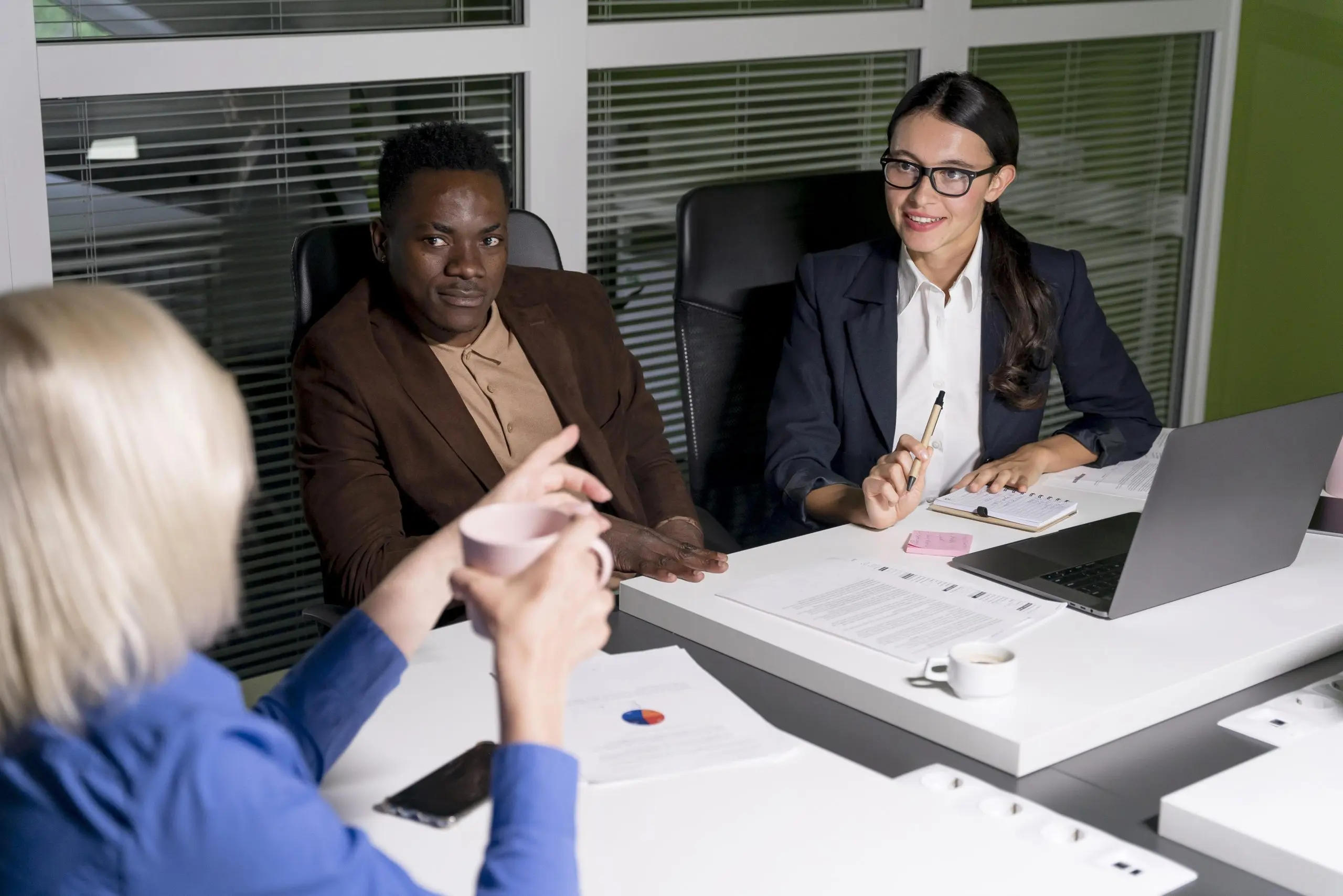 3 person having a business meeting in a room sitting on a table.